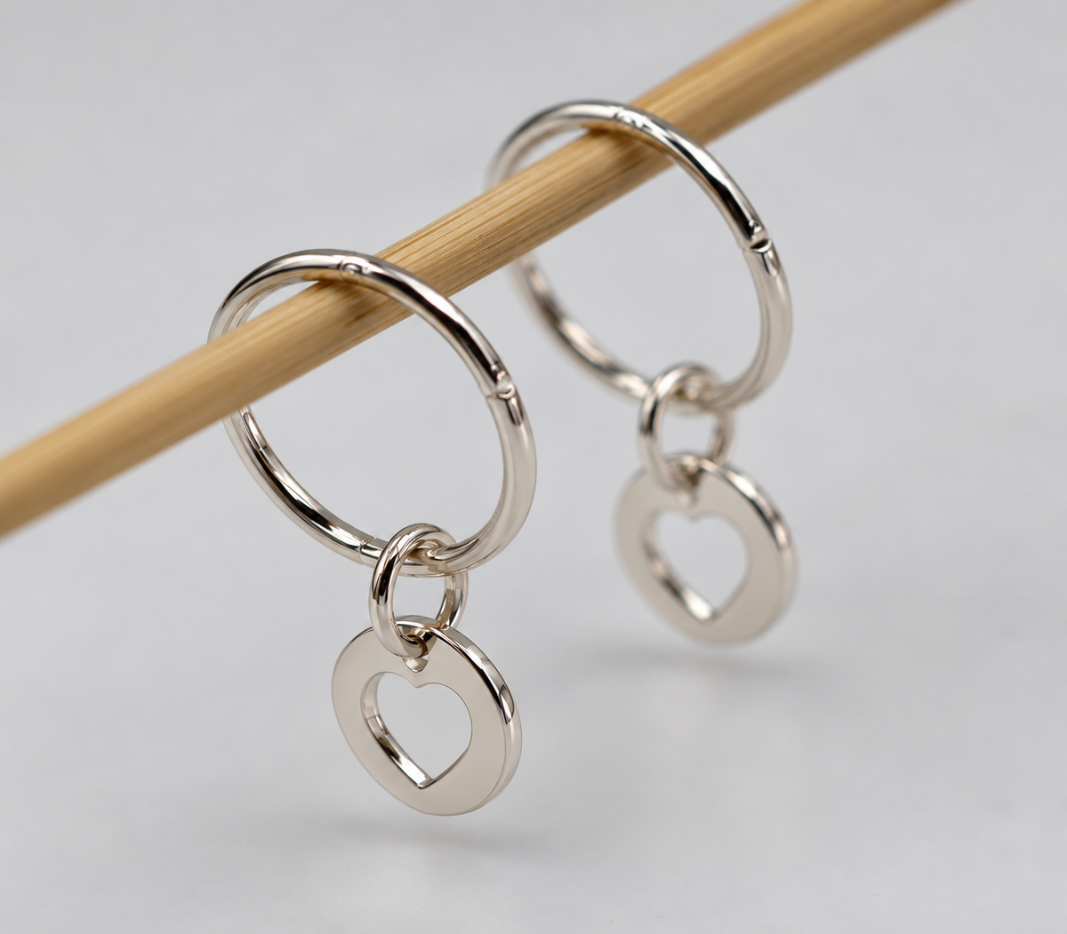 Sterling silver hinged hoop earrings with open-heart charms hanging from a wooden rod